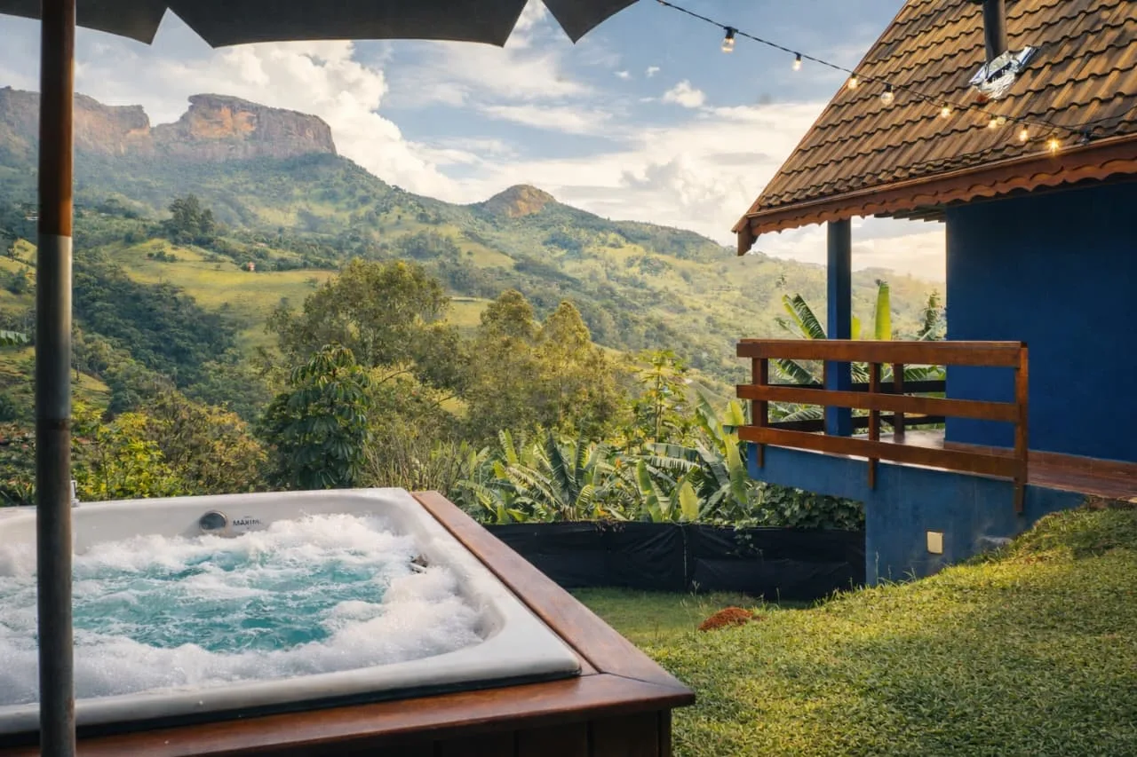 Hidromassagem na varanda do chalé, com a fachada azul e a paisagem de montanhas da Serra da Mantiqueira ao fundo